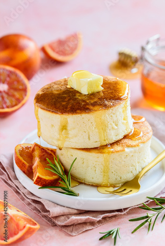 Fluffy Japanese Soufflé pancakes with honey and red oranges on a white plate. Asian food. Pink background. Selective focus
