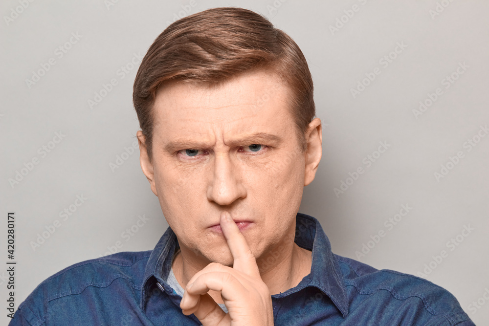 Portrait of disgruntled strict man showing silence gesture over lips Portrait of disgruntled strict man showing silence gesture over lips