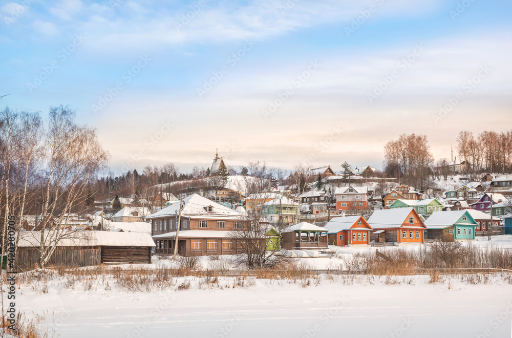 Fototapeta premium Wooden houses on the banks of the snow-covered Shokhonka River in Plyos