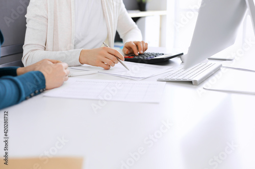 Accountant checking financial statement or counting by calculator income for tax form, hands close-up. Business woman sitting and working with colleague at the desk in office. Audit concept