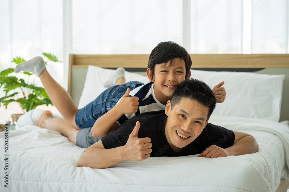 Asian young boy playing in white bed with father in new normal work from home Asian young boy playing in white bed with father in new normal work from home