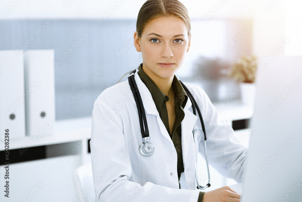 Woman-doctor typing on pc computer while sitting in sunny hospital office. Data in medicine and healthcare Woman-doctor typing on pc computer while sitting in sunny hospital office. Data in medicine and healthcare