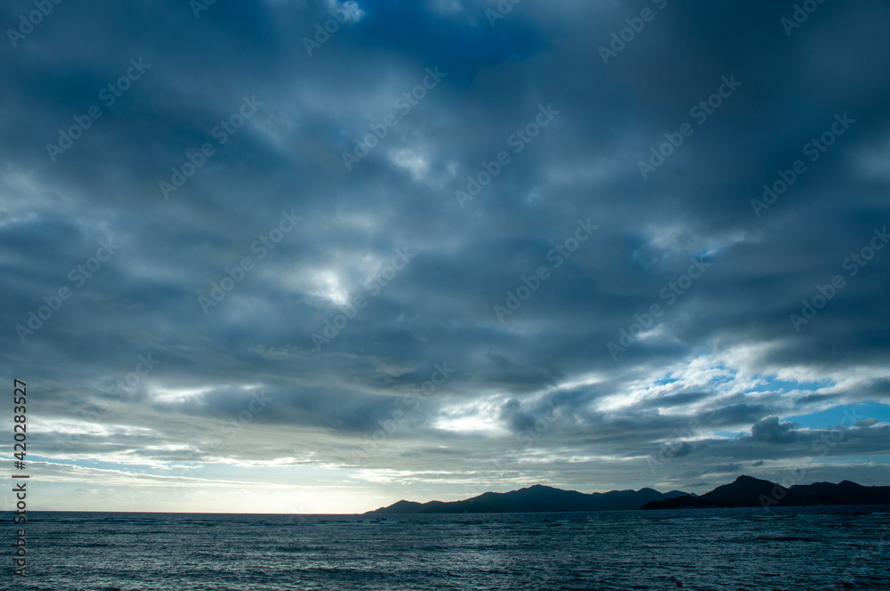 Cloudscape. Overcast sky over the ocean with silhouette of a tropical island