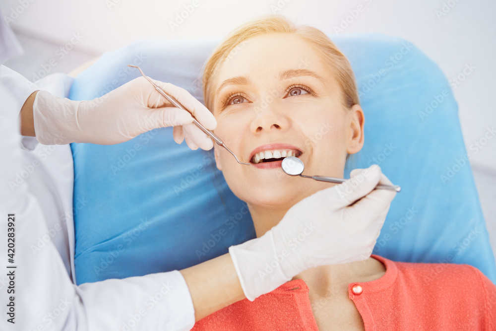 Happy smiling woman is being examined by dentist at dental clinic. Healthy teeth and medicine, stomatology concept Happy smiling woman is being examined by dentist at dental clinic. Healthy teeth and medicine, stomatology concept