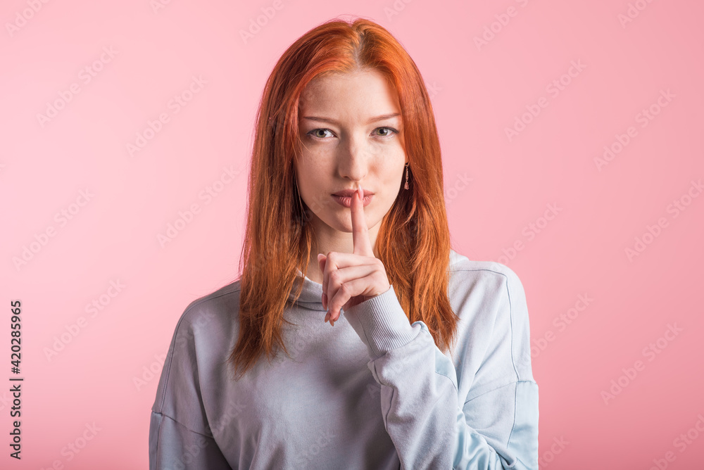 Redhead girl showing silence gesture in studio on pink background Redhead girl showing silence gesture in studio on pink background