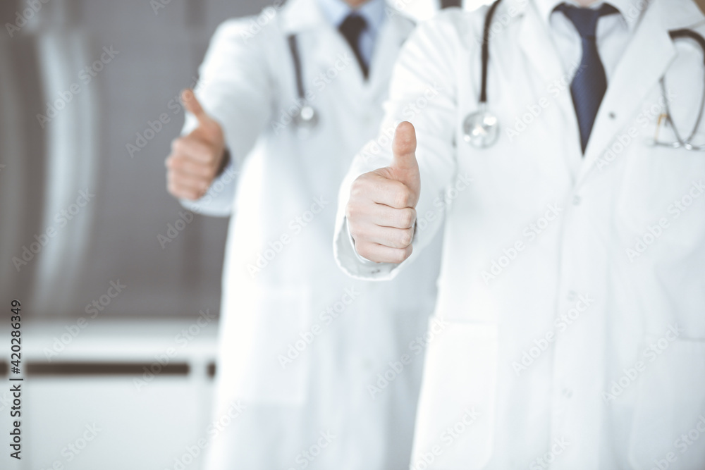 Group of modern doctors standing as a team with thumbs up or Ok sign in hospital office, close-up. Medical help, insurance in health care and medicine concept Group of modern doctors standing as a team with thumbs up or Ok sign in hospital office, close-up. Medical help, insurance in health care and medicine concept