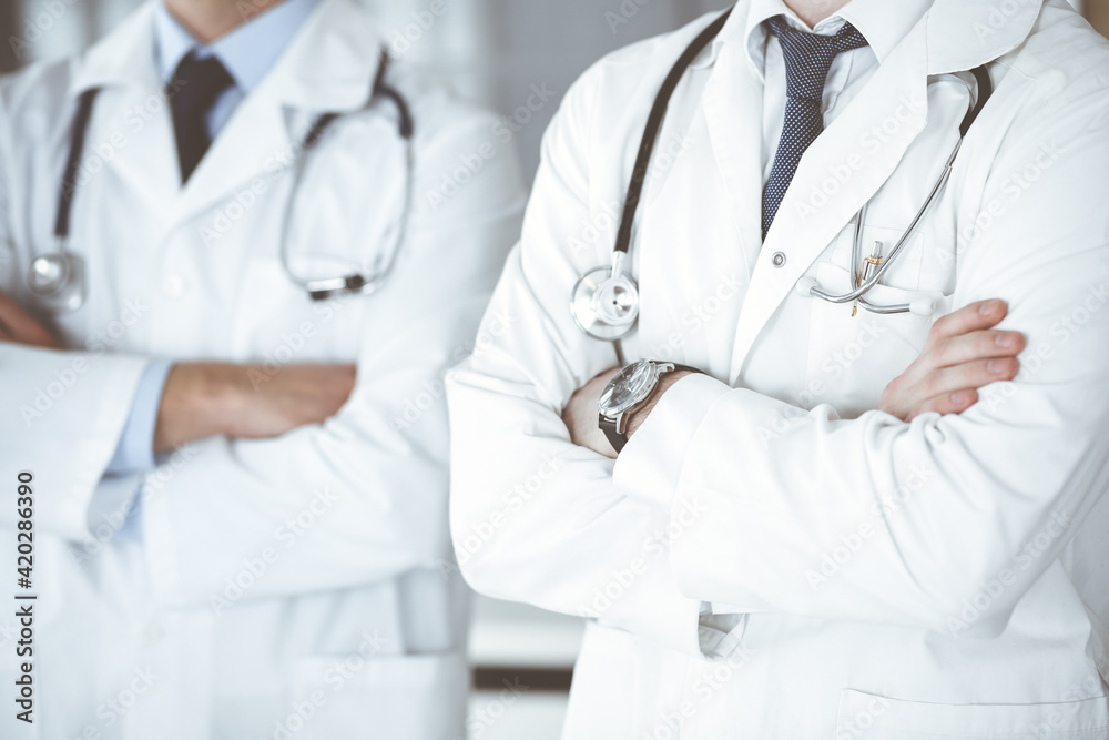 Group of unknown doctors standing as a team with arms crossed in hospital office, close-up. Medical help, insurance in health care and medicine concept