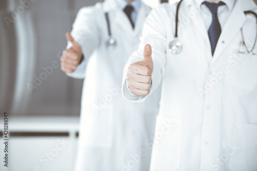 Group of modern doctors standing as a team with thumbs up or Ok sign in hospital office, close-up. Medical help, insurance in health care and medicine concept