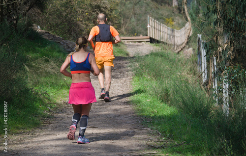 Mulher a praticar trail runnig com um homem na frente - ambiente de trilho de serra - equipamentos rosa, azul e laranja - exercicio fisico - aventura photo