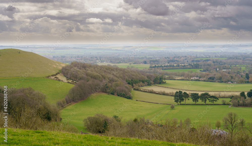 scenic Southerly view over Oare and across the Pewsey Vale valley with green pastures and a cloudy light grey sky scenic Southerly view over Oare and across the Pewsey Vale valley with green pastures and a cloudy light grey sky