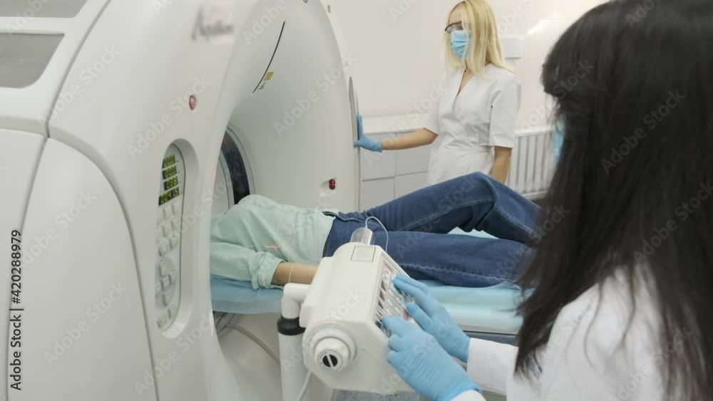 Two radiologists inserts an intravenous catheter to inject contrast to female patient who is undergoing CT or MRI scan. Patient lying on a CT or MRI scan bed, moving inside the machine. Two radiologists inserts an intravenous catheter to inject contrast to female patient who is undergoing CT or MRI scan. Patient lying on a CT or MRI scan bed, moving inside the machine.