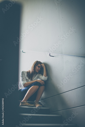 Depressed young woman sitting in a staircase, jobloss due to coronavirus pandemic, Covid-19 outbreak. Unemployment, economic crisis, financial distress concept photo