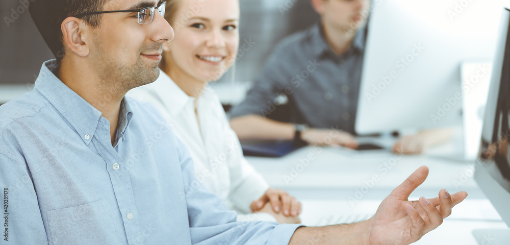 Business people working together in modern office. Happy smiling adult businessman using pc computer with colleagues. Teamwork and partnership concept Business people working together in modern office. Happy smiling adult businessman using pc computer with colleagues. Teamwork and partnership concept