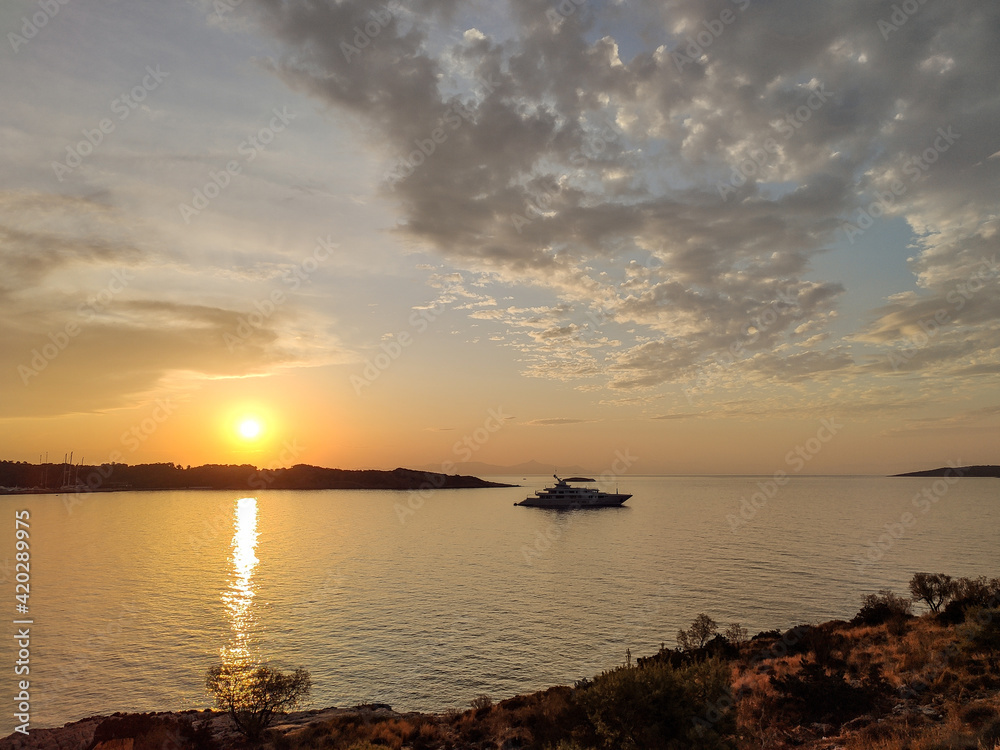 Orange sunset sun shining above Greek islands in Aegean sea in Greece. Summer tourism travel. Scenic clouds and yacht in calm sea in evening