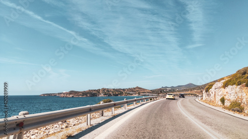 Fototapeta Naklejka Na Ścianę i Meble -  Sunny road driving on coastline of Aegean sea in Greece. Summer tourism travel. Scenic bright color graded day car drive vacation