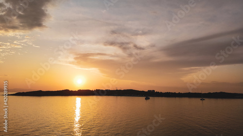 Orange sunset sun shining above Greek islands in Aegean sea near Athens in Greece. Summer tourism travel. Scenic clouds and yachts in calm sea in evening