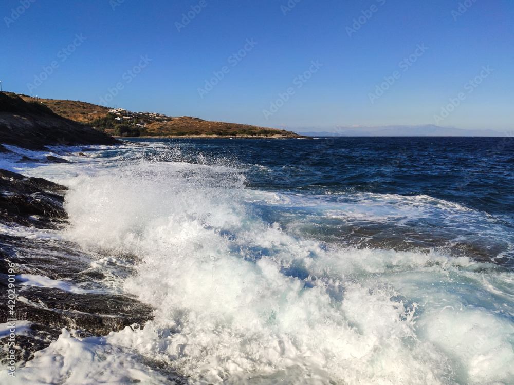 Powerful wave splash on stormy blue sea breaking rocky shore. Summer sunny day on sea with white waves on Aegean sea in Greece Powerful wave splash on stormy blue sea breaking rocky shore. Summer sunny day on sea with white waves on Aegean sea in Greece