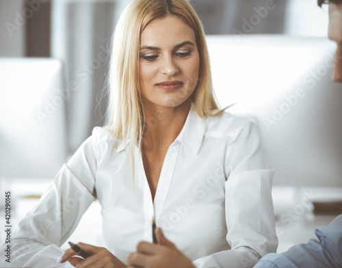 Group of business people discussing questions at meeting. Headshot of blonde businesswoman while smiling to her colleague at office negotiation. Teamwork and cooperation in corporate occupation