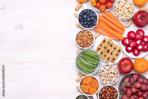 Healthy snacks such as fresh fruits, vegetables and nuts on white wooden table, top view with copy space