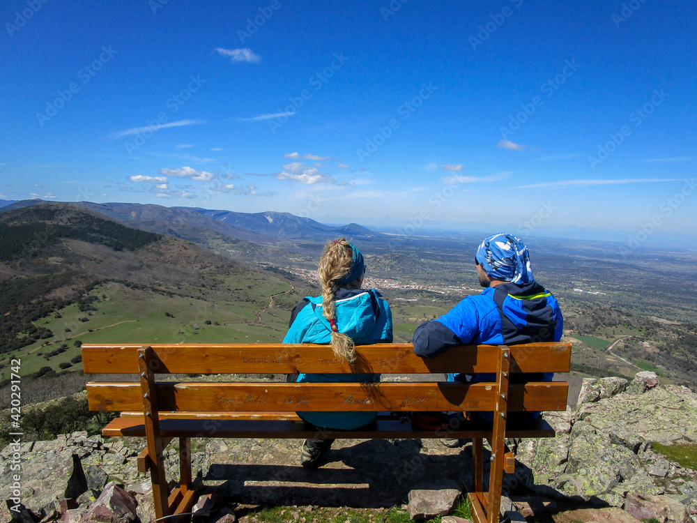 COUPLE SITTING ON A WOODEN BENCH AT THE TOP OF THE MOUNTAIN