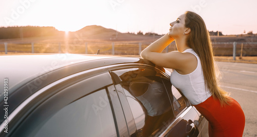 Beautiful young girl near a car in the evening in the sunset sun in an empty parking lot