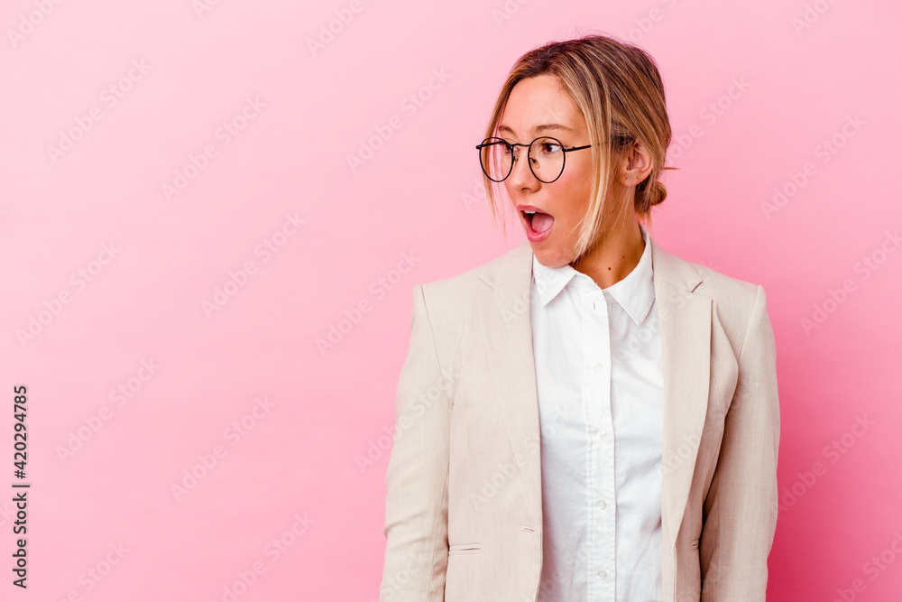 Young caucasian mixed race business woman isolated on pink background being shocked because of something she has seen.