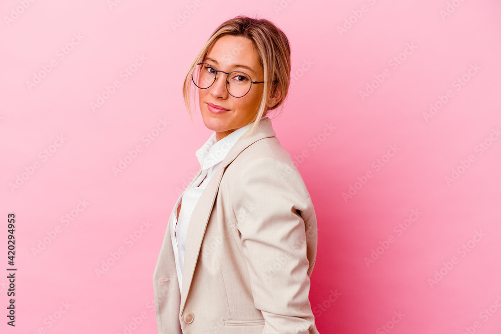 Young caucasian mixed race business woman isolated on pink background looks aside smiling, cheerful and pleasant.