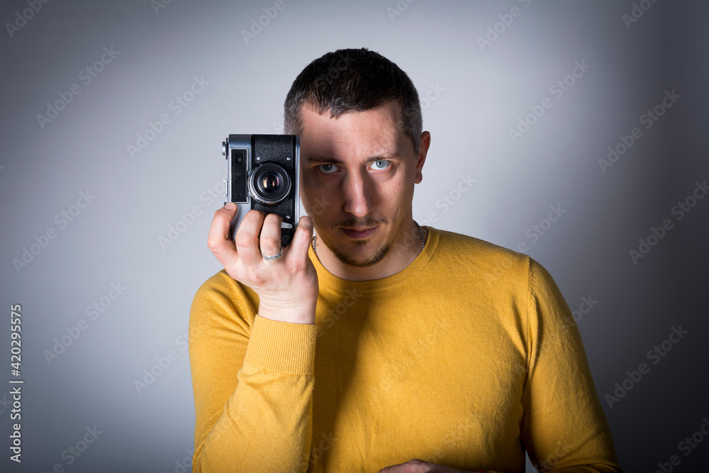 A man in a yellow sweater poses with a vintage film camera A man in a yellow sweater poses with a vintage film camera