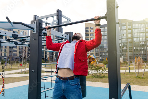 A guy in casual clothes pulls up on a horizontal bar in the courtyard of a residential quarter