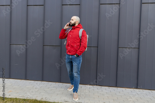 Portrait of a brutal guy with a beard in casual clothes who is talking on the phone on the street