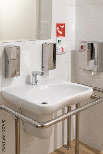 A sink with a mirror  a dispenser for soap  a SOS call button for staff in the toilet room for the elderly and disabled