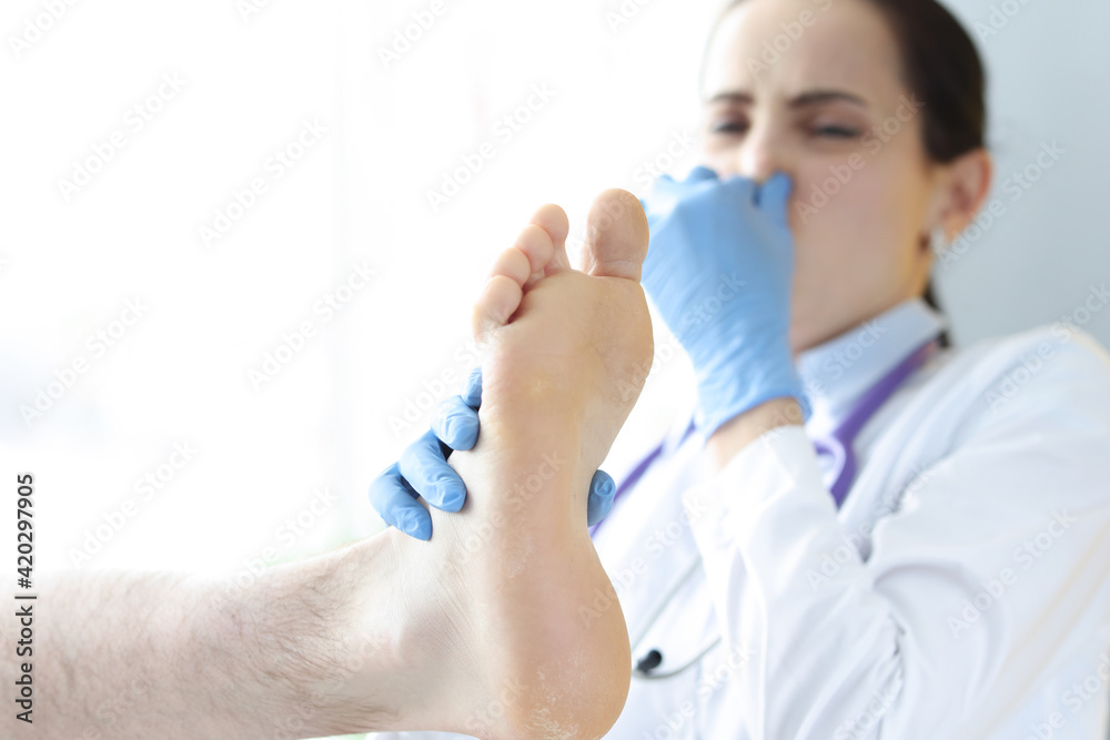 Doctor covers nose from unpleasant smell from male leg Doctor covers nose from unpleasant smell from male leg