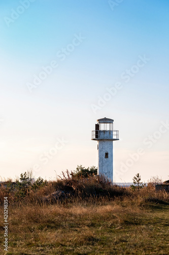 White  abandoned  empty  old lighthouse on sea coast. Spring  summer or autumn shore landscape with lighthouse fragment against blue sky background. Building remains. Copy space