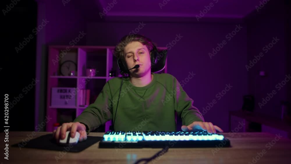 Funny young man in a headset on his head sleeps in a gaming chair at night at the computer. Night training gaming. Funny young man in a headset on his head sleeps in a gaming chair at night at the computer. Night training gaming.