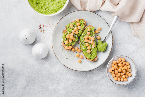 Vegan toasts with mashed avocado and chickpeas on a grey concrete background, top view. Healthy vegetarian avocado chickpea toasts garnished with hemp seeds