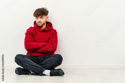 Young Moroccan man sitting on the floor isolated on white background suspicious, uncertain, examining you. © Asier