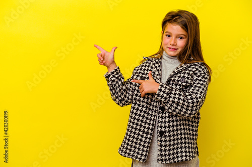Little caucasian girl isolated on yellow background pointing with forefingers to a copy space, expressing excitement and desire.