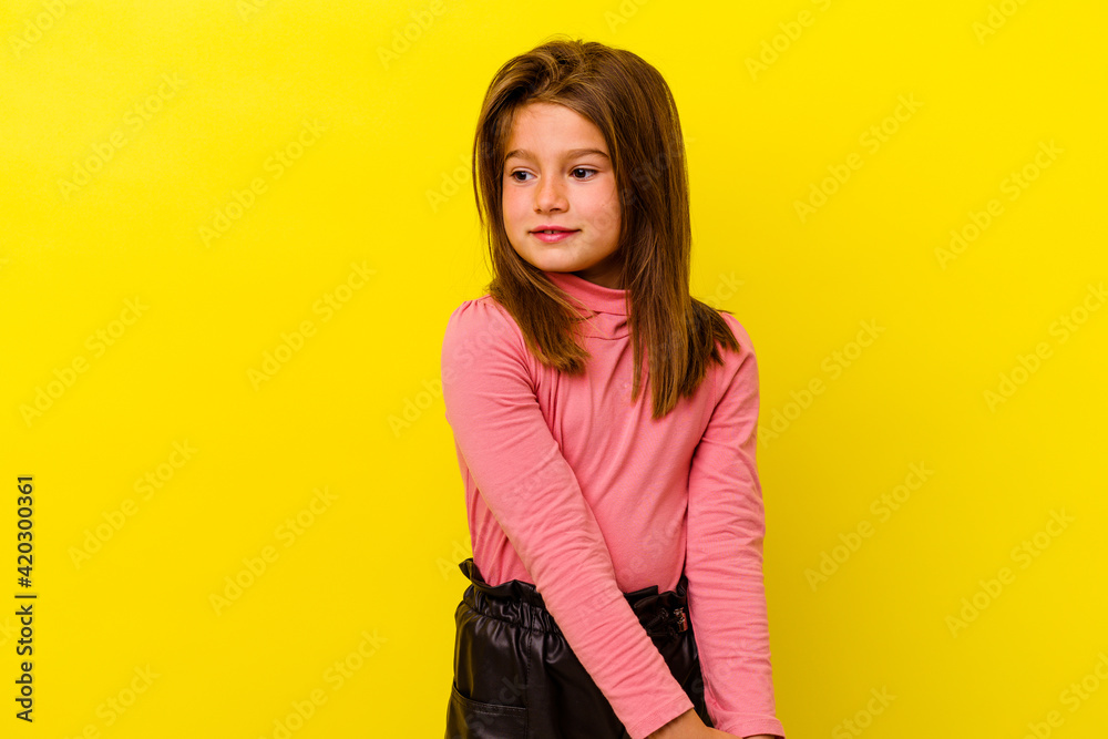 Little caucasian girl isolated on yellow background looks aside smiling, cheerful and pleasant.