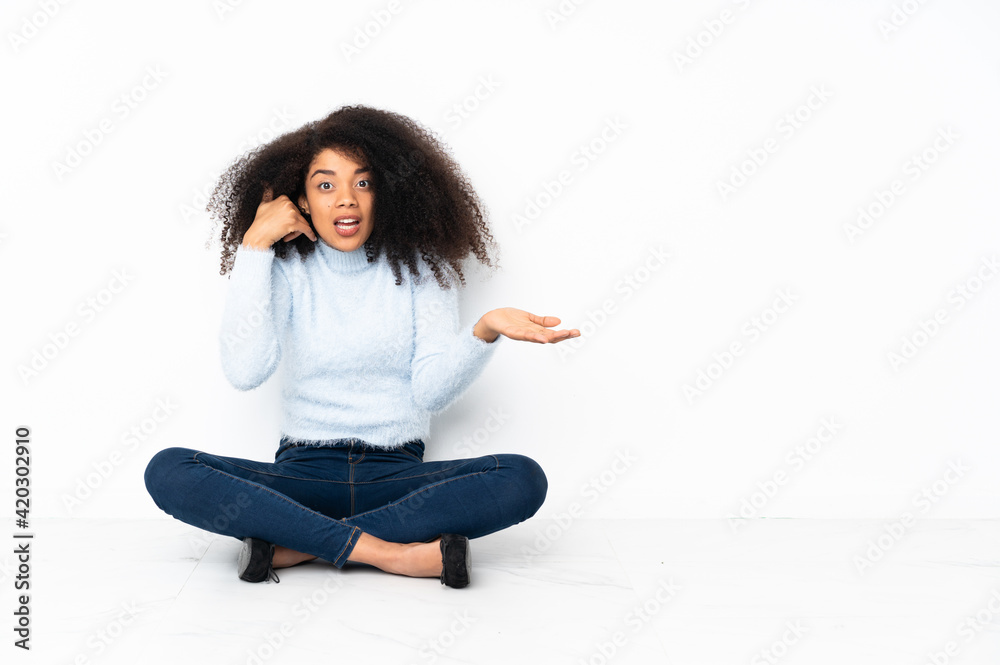 Young african american woman sitting on the floor making phone gesture and doubting Young african american woman sitting on the floor making phone gesture and doubting