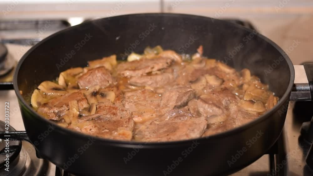 A cook prepares roasted meat with mushrooms in the kitchen. A cook prepares roasted meat with mushrooms in the kitchen.