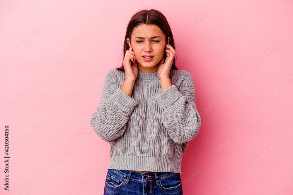 Young Indian woman isolated on pink background covering ears with fingers, stressed and desperate by a loudly ambient. Young Indian woman isolated on pink background covering ears with fingers, stressed and desperate by a loudly ambient.
