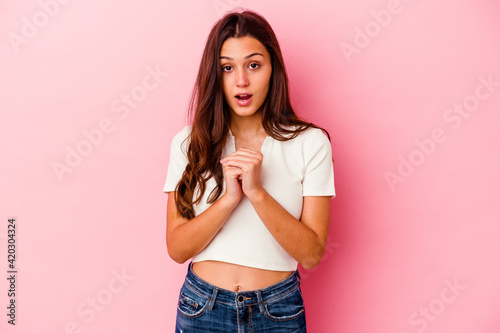 Young Indian woman isolated on pink background praying for luck, amazed and opening mouth looking to front.