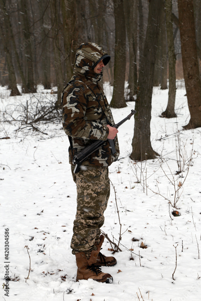 Fototapeta premium The man with machine gun in the snowy forest
