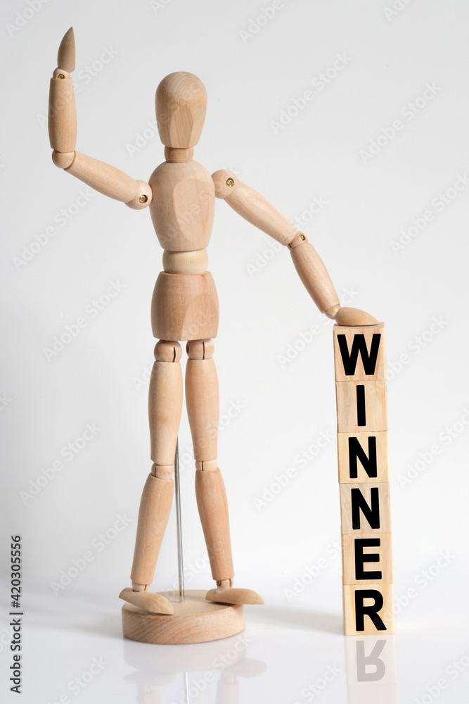 The wooden man raised his hand, and under his left hand he has cubes with the inscription - WINNER The wooden man raised his hand, and under his left hand he has cubes with the inscription - WINNER