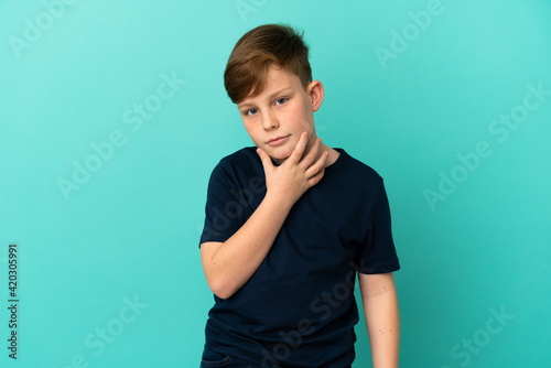 Little redhead boy isolated on blue background thinking