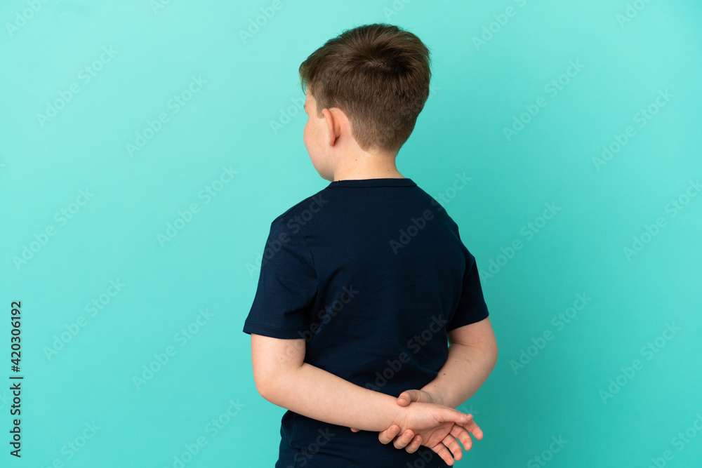 Little redhead boy isolated on blue background in back position and looking back Little redhead boy isolated on blue background in back position and looking back