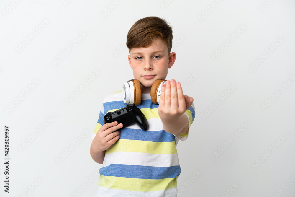 Little redhead boy holding a game pad isolated on white background inviting to come with hand. Happy that you came Little redhead boy holding a game pad isolated on white background inviting to come with hand. Happy that you came