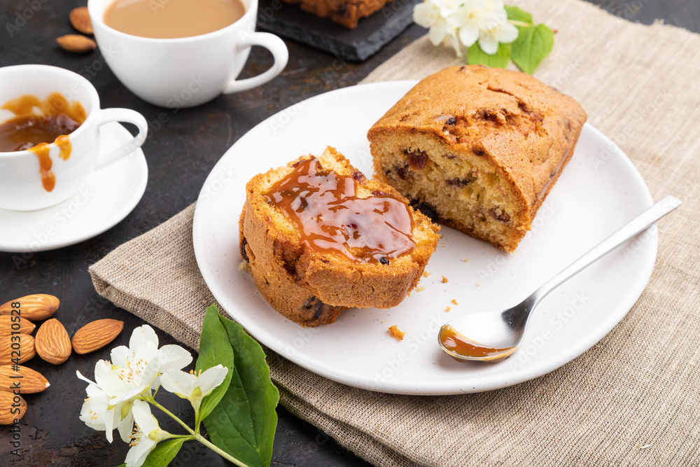 Homemade cake with raisins, almonds, soft caramel and a cup of coffee on a black concrete background. Side view, close up. Homemade cake with raisins, almonds, soft caramel and a cup of coffee on a black concrete background. Side view, close up.