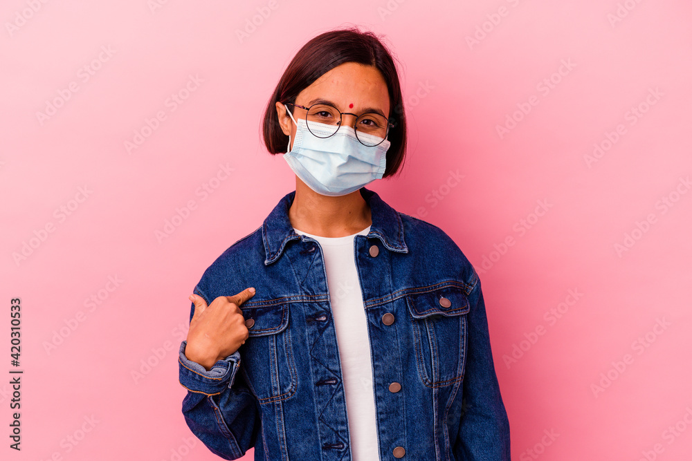 Young Indian woman wearing a mask antivirus isolated on pink background person pointing by hand to a shirt copy space, proud and confident