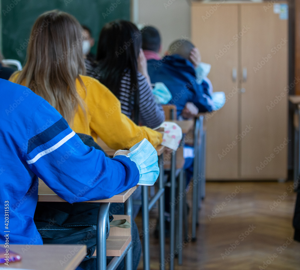 School boy sitting in classroom with mask on hand School boy sitting in classroom with mask on hand